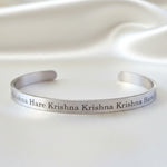 A stainless steel bracelet with the Krishna Maha Mantra displayed against a satin background.