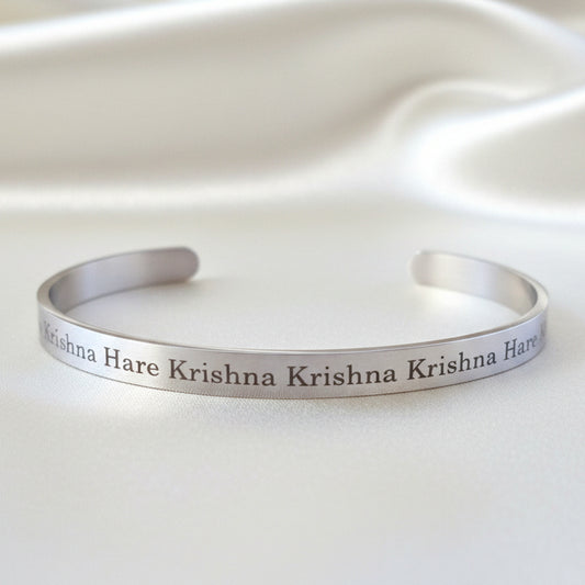 A stainless steel bracelet with the Krishna Maha Mantra displayed against a satin background.