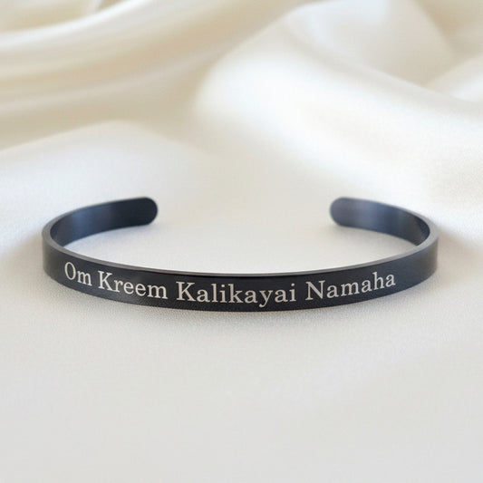 Black Kali Mantra bracelet with engraved text on a textured beige surface