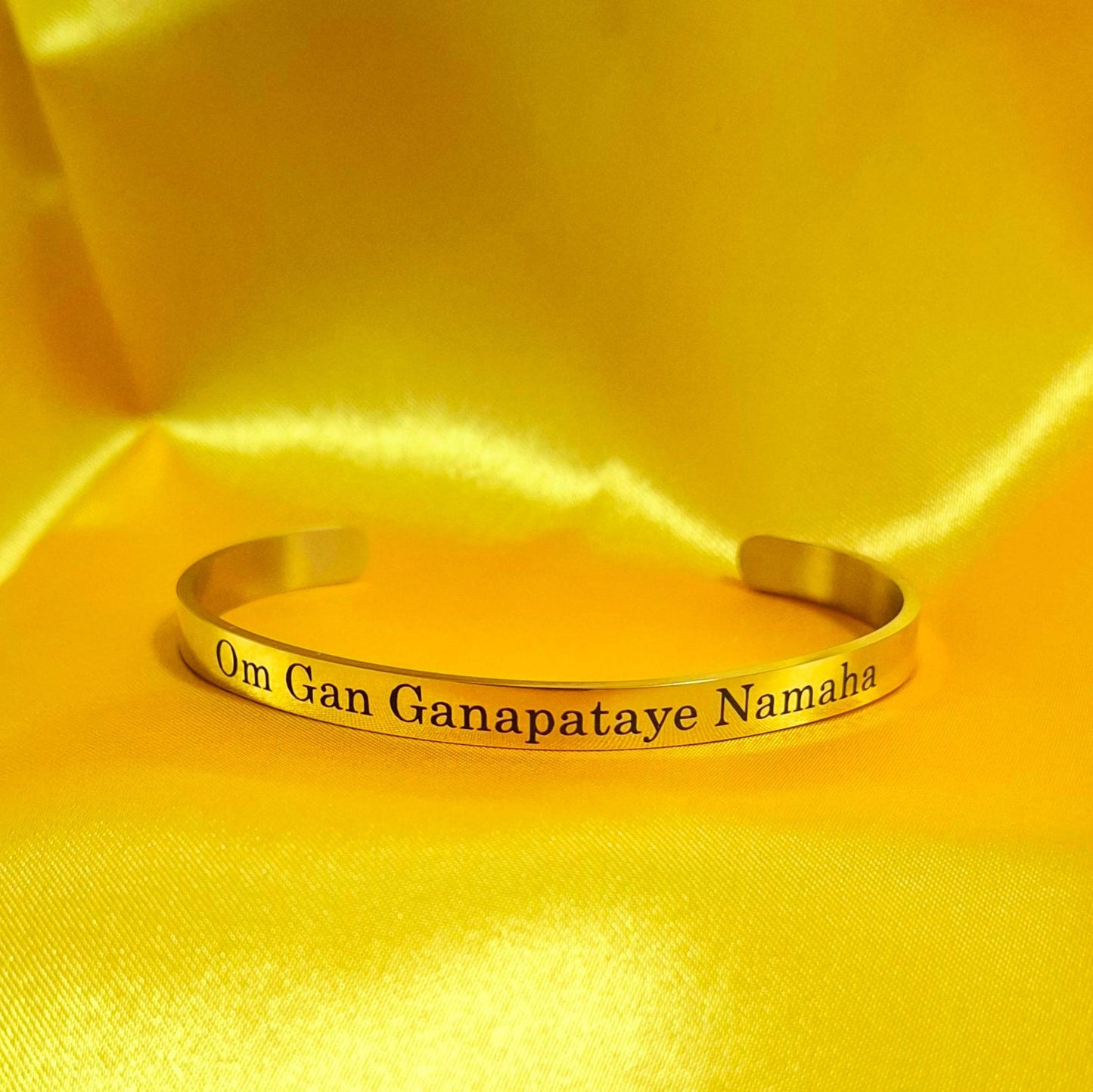 Golden finish Lord Ganesha bracelet with engraved text on a yellow satin background
