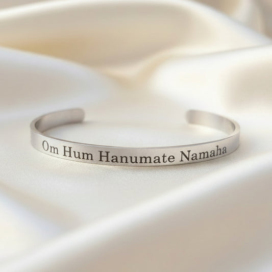 A silver-finished bracelet with the text 'Om Hanumate Namah' engraved on it, displayed on a textured background.
