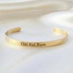 Gold bracelet with 'Om Sai Ram' engraving on a fabric background